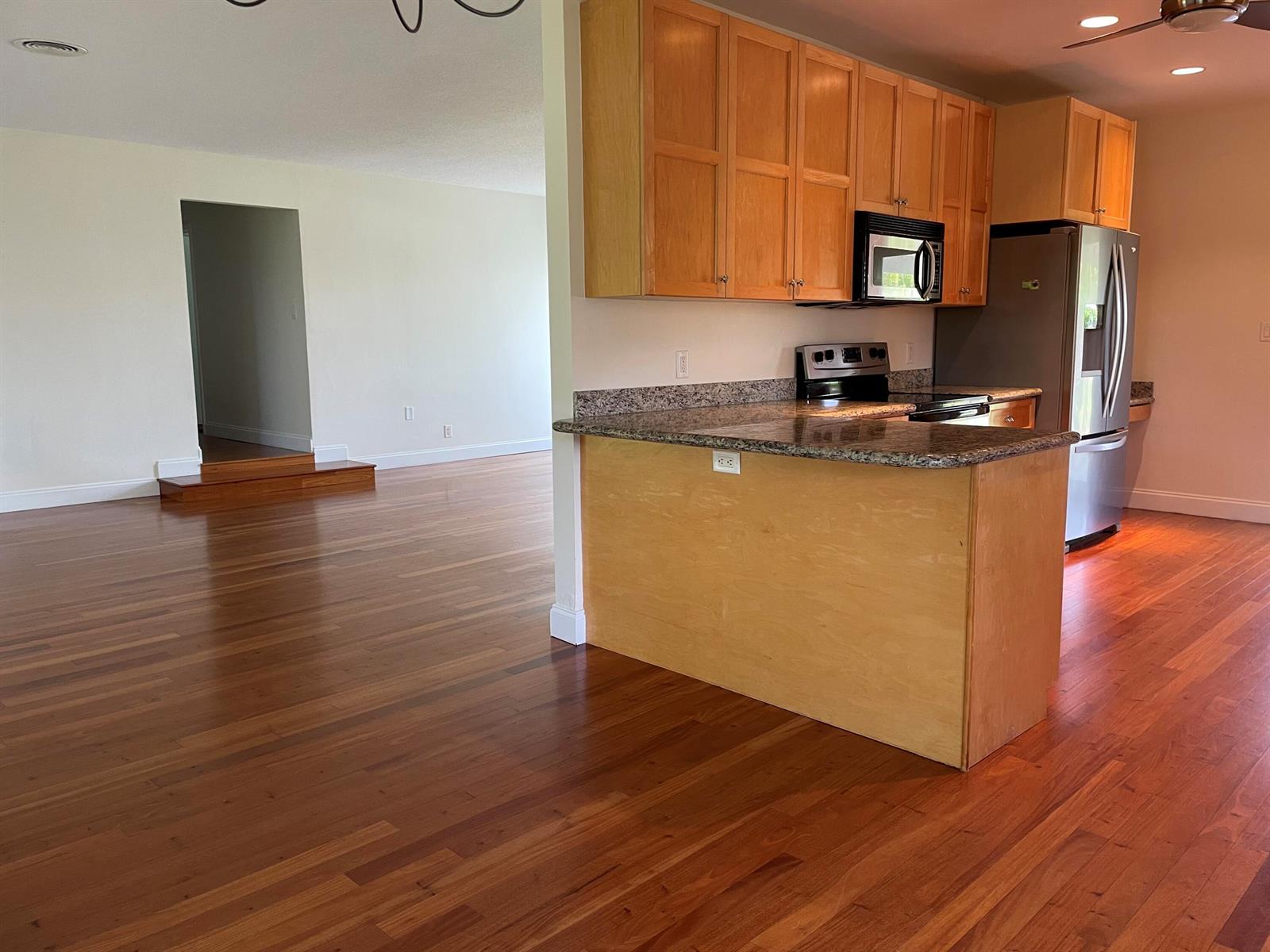 A kitchen with light wood cabinets and granite countertops overlooks a hardwood-floored living area — 465 NE 34th Street, Boca Raton FL 33431, BOCA RATON, FL
