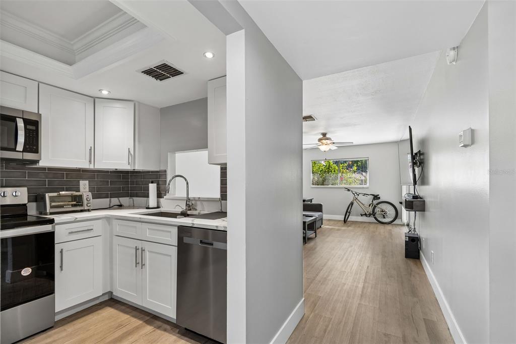 A modern kitchen with white cabinets and stainless steel appliances opens into a living area — 2460 NORTHSIDE DRIVE UNIT 604, CLEARWATER, FL