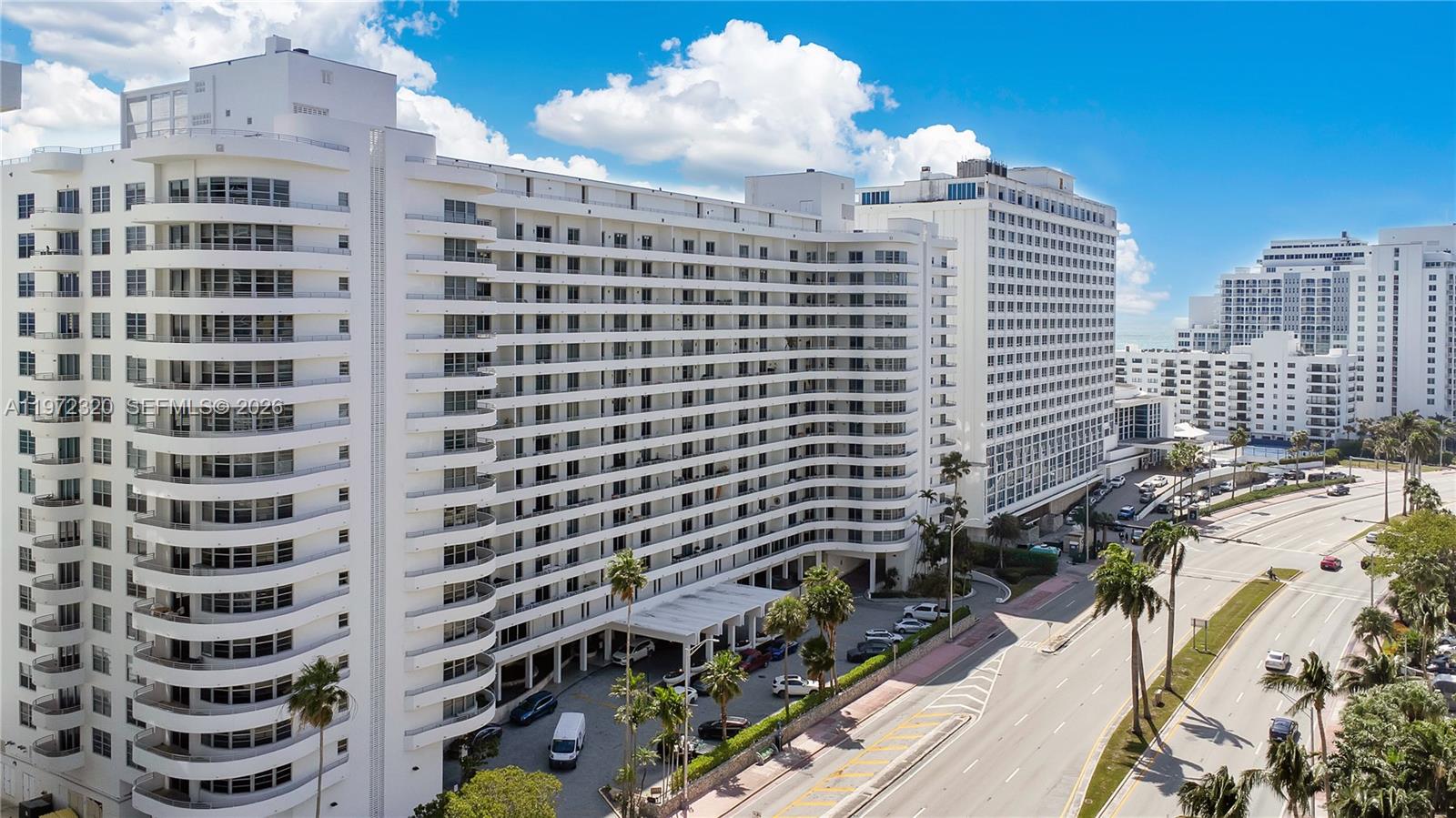 An aerial view of a large white multi-story apartment building next to a multi-lane road — 5555 Collins Ave # 5B, Miami Beach FL 33140, MIAMI BEACH, FL