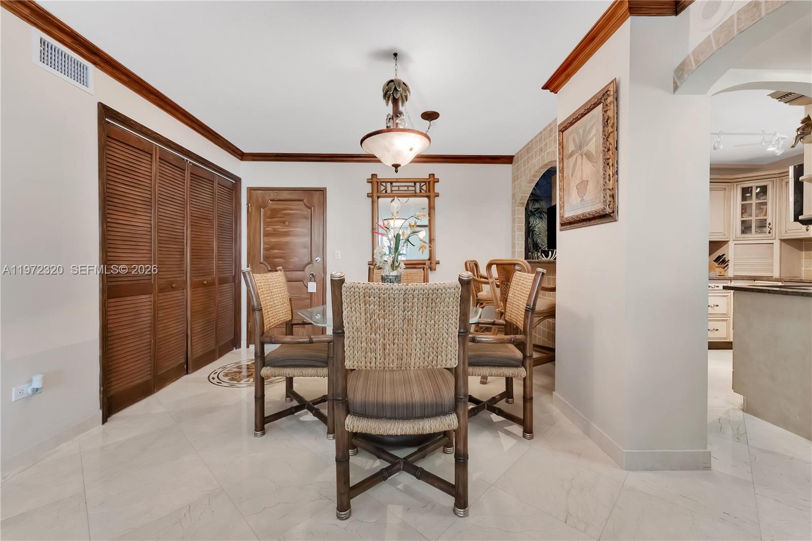 A dining area features a glass table, bamboo-style chairs, and a chandelier on tile floors — 5555 Collins Ave # 5B, Miami Beach FL 33140, MIAMI BEACH, FL