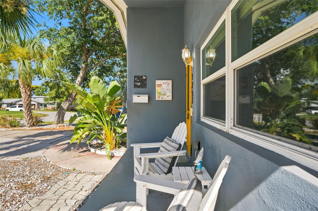 A covered front porch features two white Adirondack chairs, a small table, and a yellow door — 1257 FRANKLIN STREET, CLEARWATER, FL