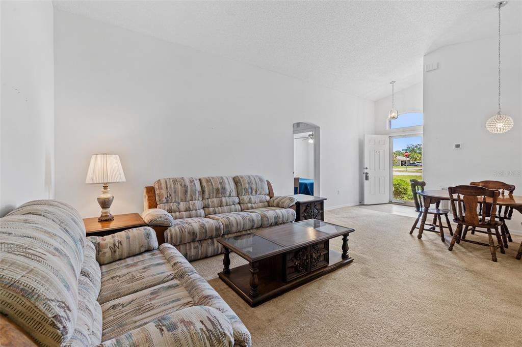 A living room with beige carpet, patterned sofas, a wooden coffee table, and an open doorway — 320 BROKEN OAK DRIVE, EDGEWATER, FL., FL