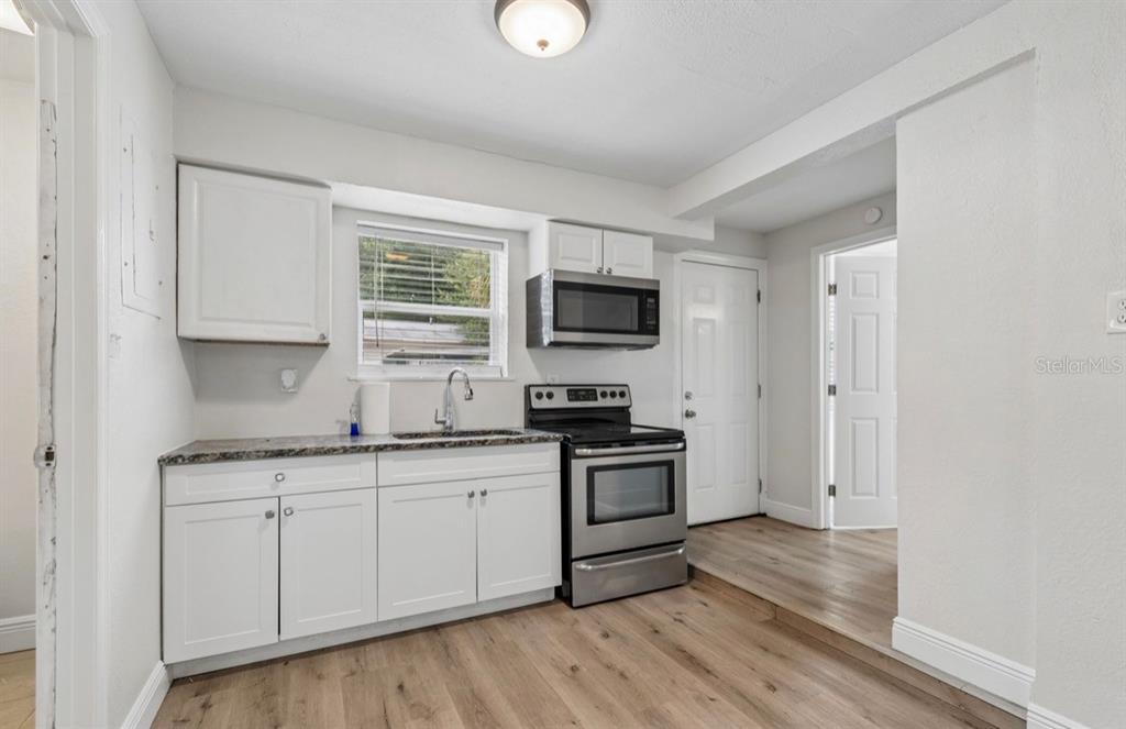 A kitchen features white cabinets, stainless steel appliances, a window, and wood-look flooring — 725 21ST AVENUE S, ST PETERSBURG, FL