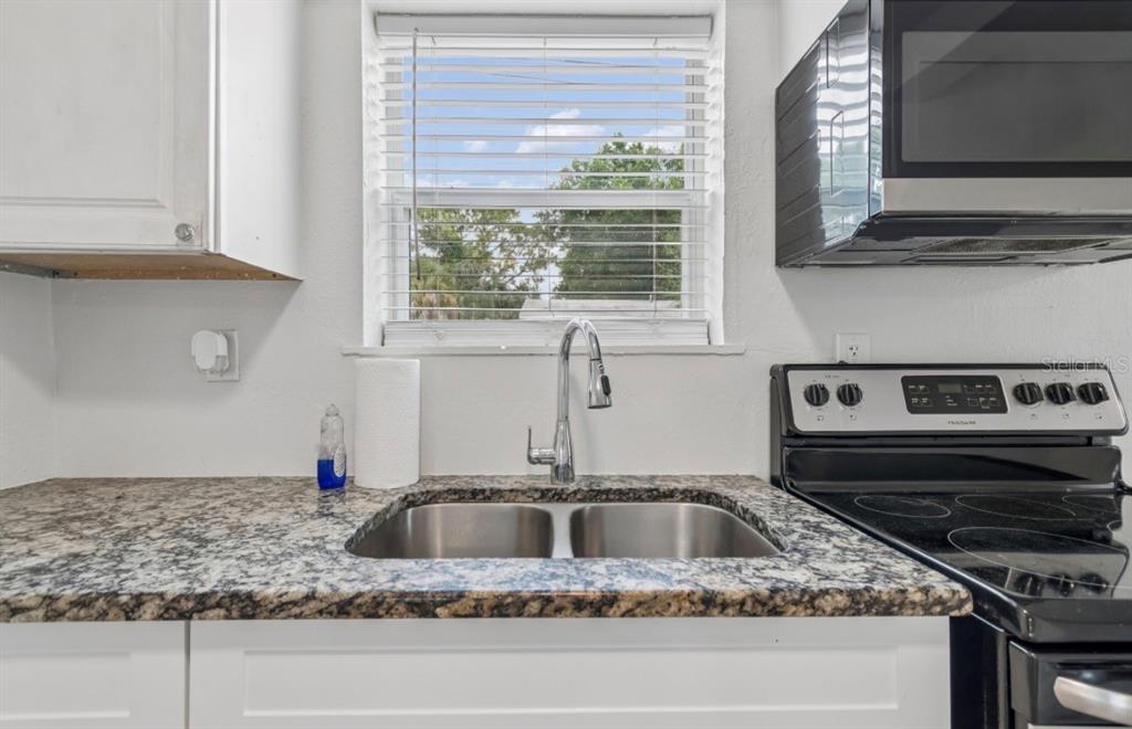 A kitchen features a double-basin stainless steel sink, granite countertops, and a window with blinds — 725 21ST AVENUE S, ST PETERSBURG, FL