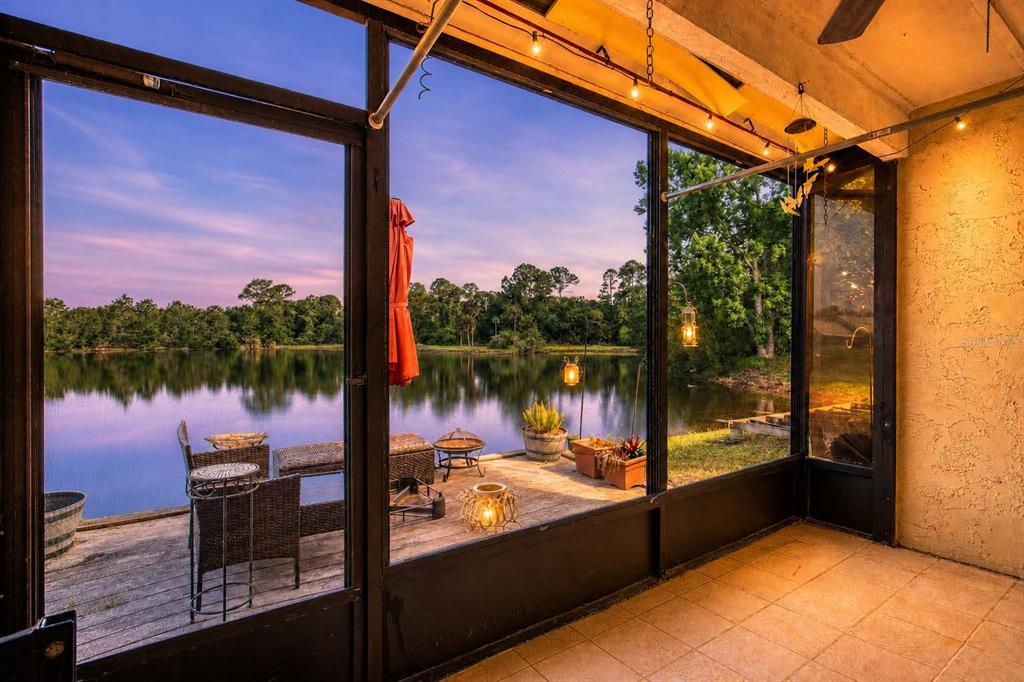 A screened-in porch overlooks a lake with a wooden deck and outdoor furniture at sunset — 210 LEMON TREE LANE UNIT 9, ORMOND BEACH, FL