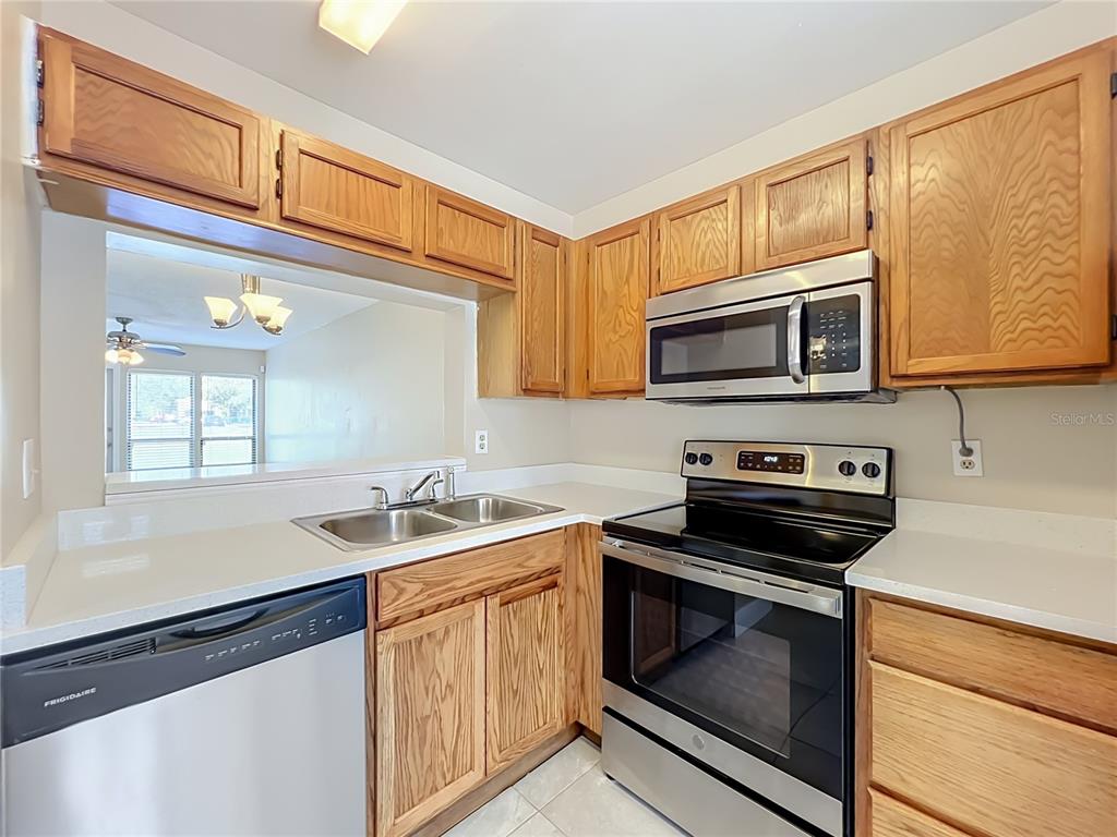 A kitchen features oak cabinets, stainless steel appliances, and a pass-through window to another room — 2234 STONINGTON AVENUE UNIT 2234, ORLANDO, FL