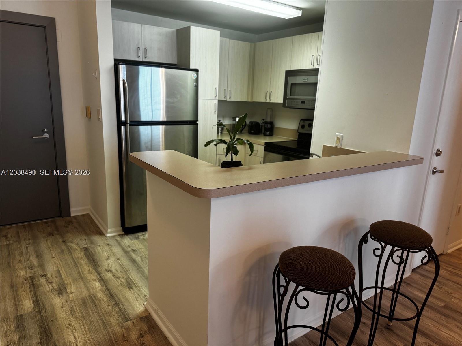 A kitchen features light wood cabinets, stainless steel appliances, and a breakfast bar with stools — 185 SE 14th Ter # 1812, Miami FL 33131, MIAMI, FL