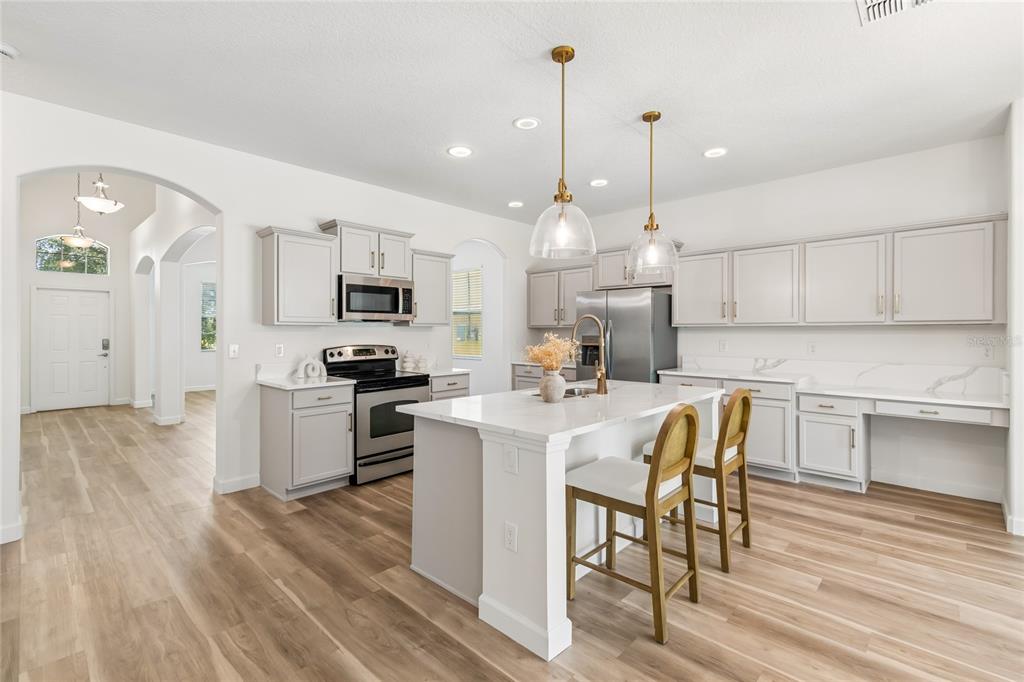 A modern kitchen features light gray cabinets, a white quartz island, and wood-look flooring — 12410 LATCHFORD STREAM PLACE, RIVERVIEW, FL