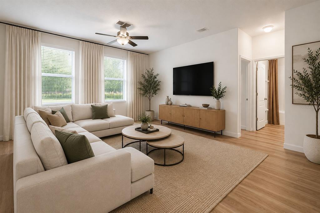 A living room features a beige sectional sofa, nested coffee tables, and a wall-mounted television — 12410 LATCHFORD STREAM PLACE, RIVERVIEW, FL