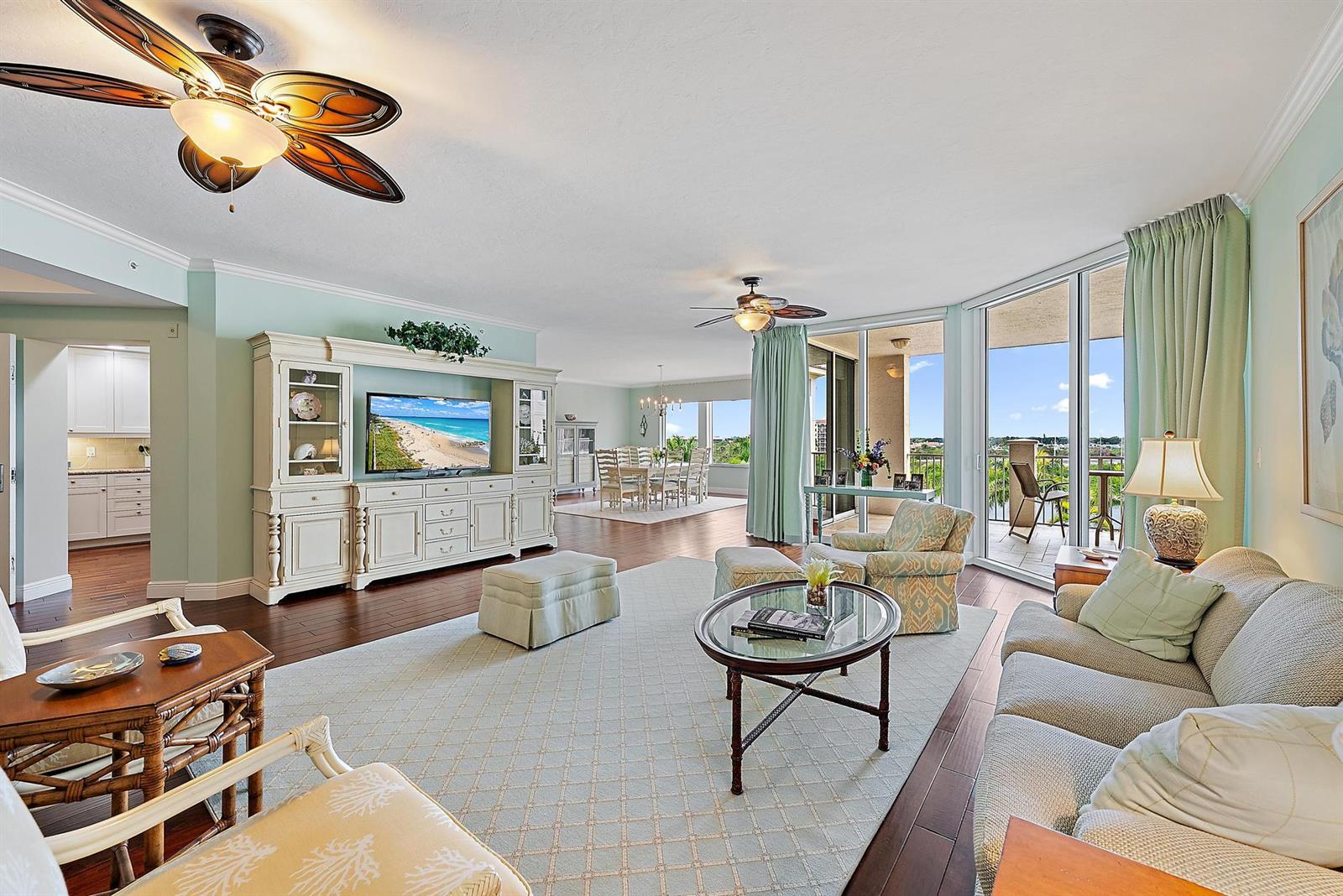A spacious living room features light green walls, hardwood floors, a large entertainment center, and balcony access — 700 S Us Highway 1 # 406, Jupiter FL 33477, JUPITER, FL