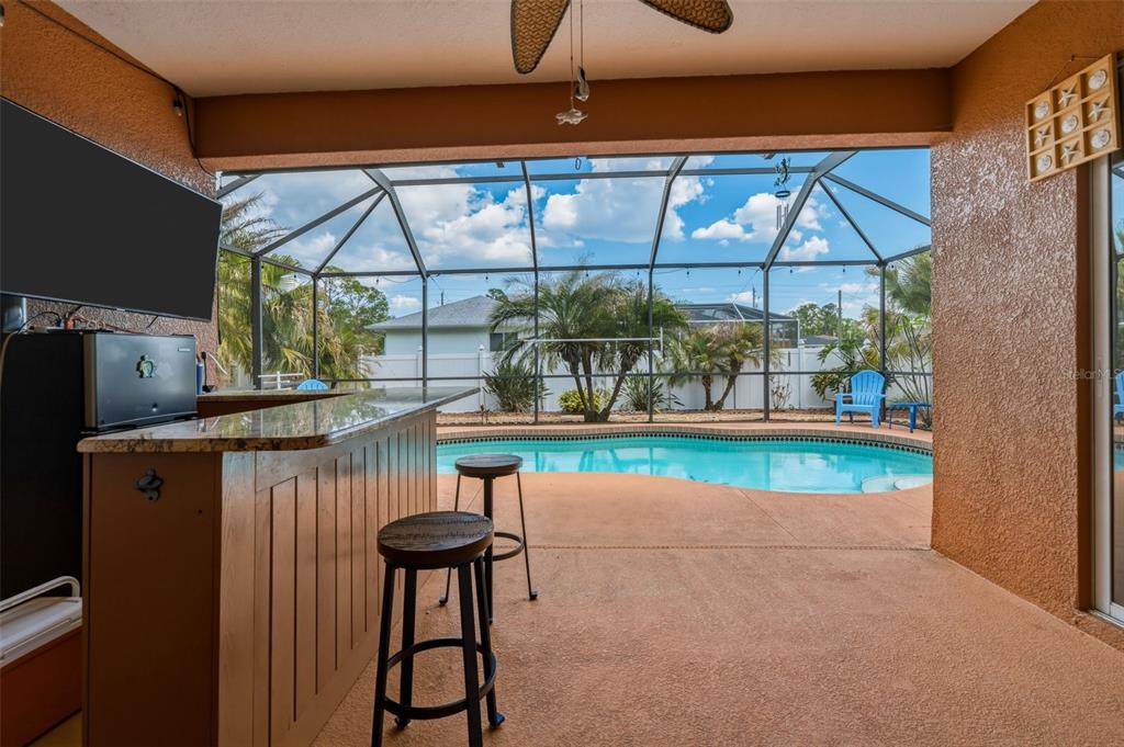 A covered patio features a wooden bar with stools, a television, and a screened-in pool — 2486 LAWYER TERRACE, NORTH PORT, FL