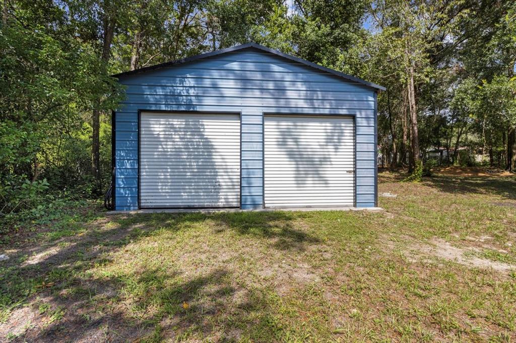 A blue metal two-car garage stands in a wooded, grassy yard — 5700 S CALGARY TERRACE, INVERNESS, FL