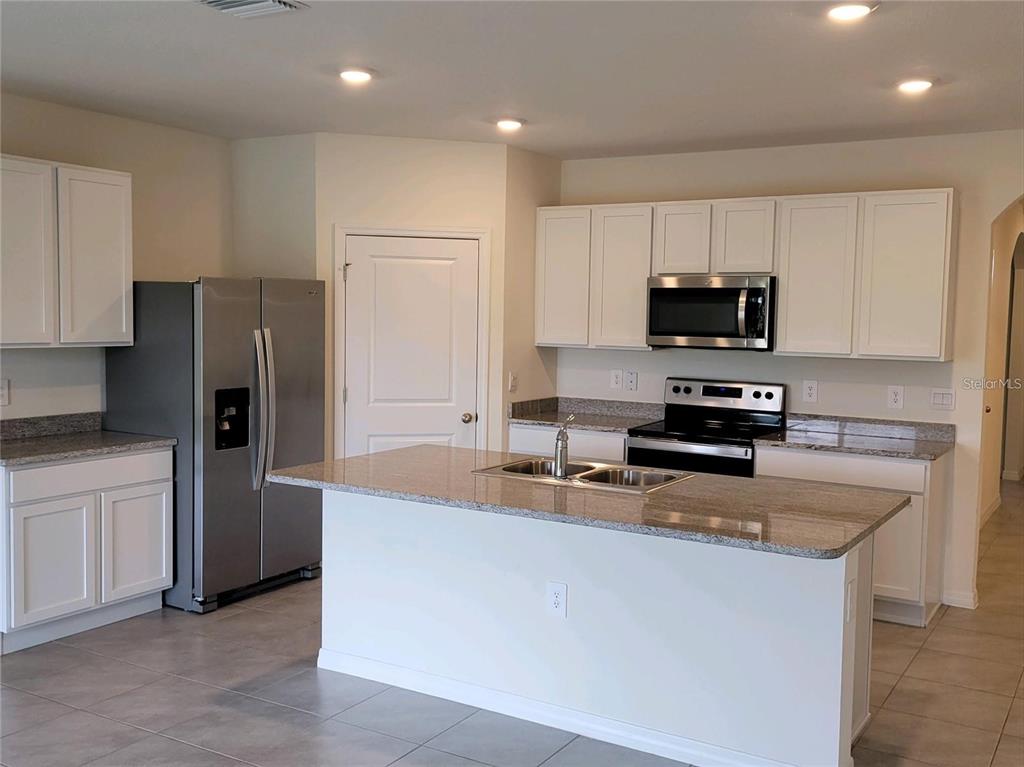 A kitchen features white cabinets, granite countertops, stainless steel appliances, and a central island — 17419 HARVEST MOON WAY, BRADENTON, FL