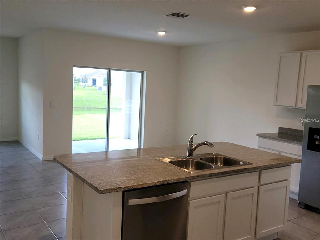 A kitchen island with a double sink and dishwasher sits before a sliding glass door — 17419 HARVEST MOON WAY, BRADENTON, FL