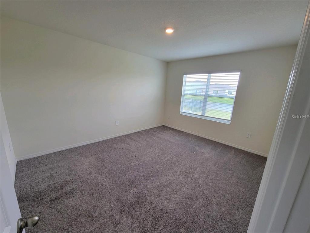 An empty bedroom features beige walls, gray carpeting, and a single window with blinds — 17419 HARVEST MOON WAY, BRADENTON, FL