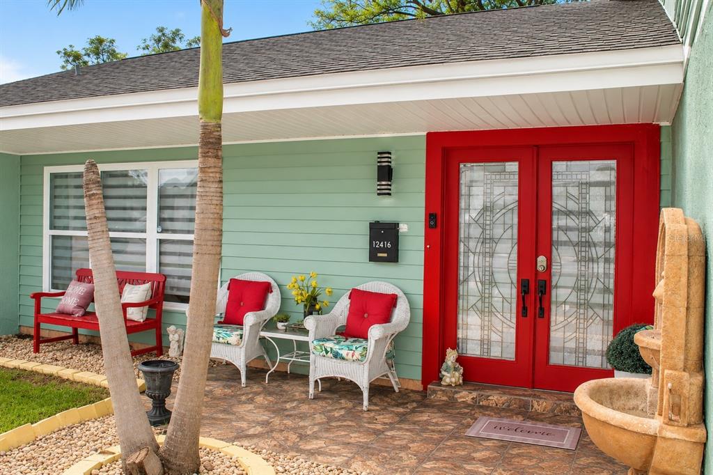 A front porch features a red double door, white wicker chairs, and a red bench — 12416 COBBLE STONE DRIVE, HUDSON, FL