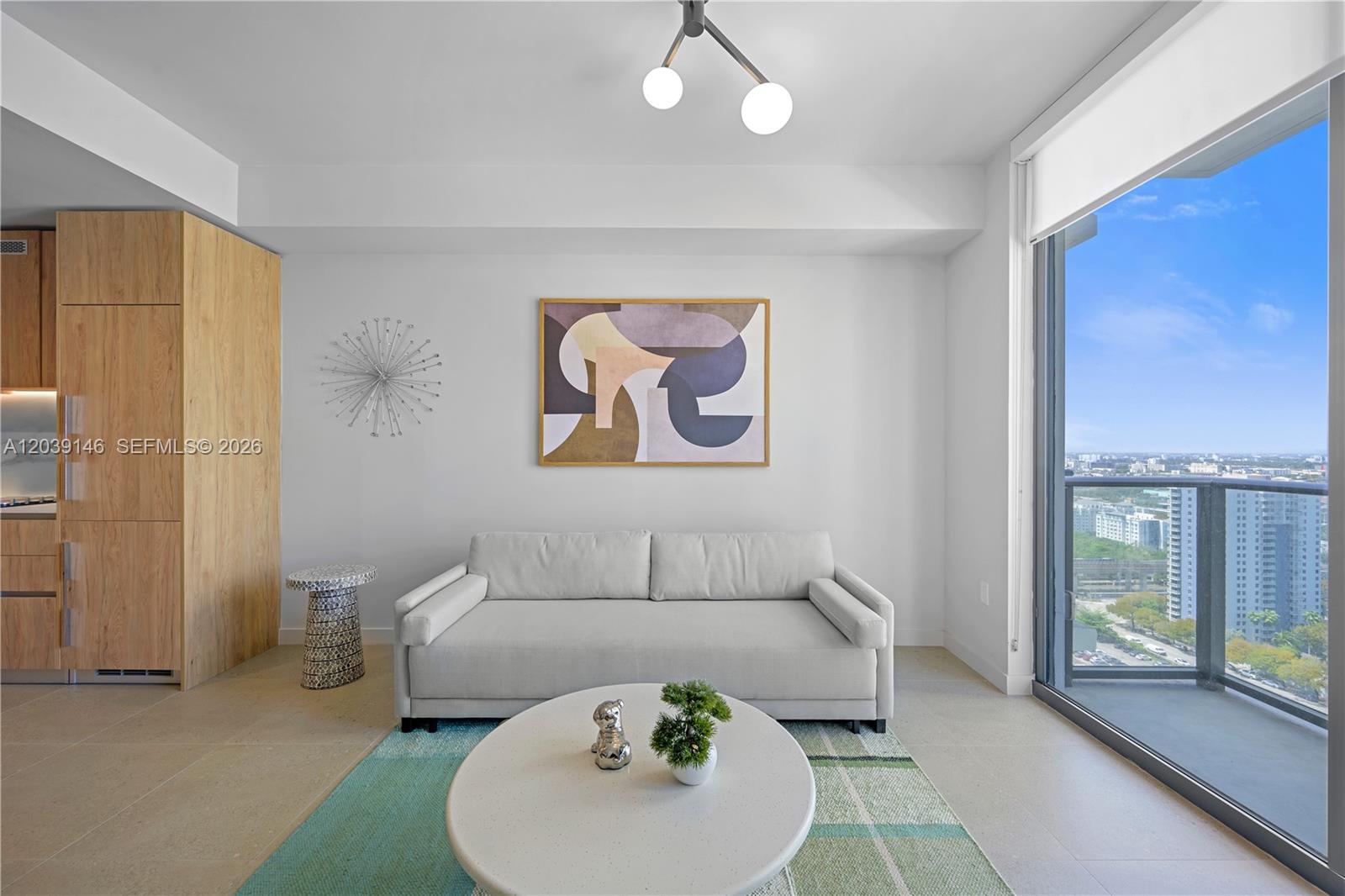 A modern living room features a light gray sofa, abstract wall art, and a balcony view — 11 NE 6th St # 1111, Miami FL 33132, MIAMI, FL