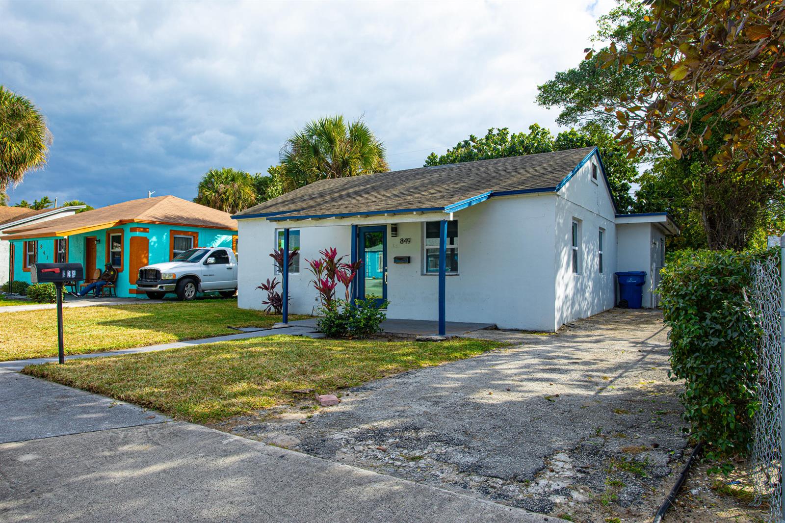 A white single-story house with a blue-trimmed porch and a driveway sits next to another house — 849 W 2nd Street, Riviera Beach FL 33404, RIVIERA BEACH, FL