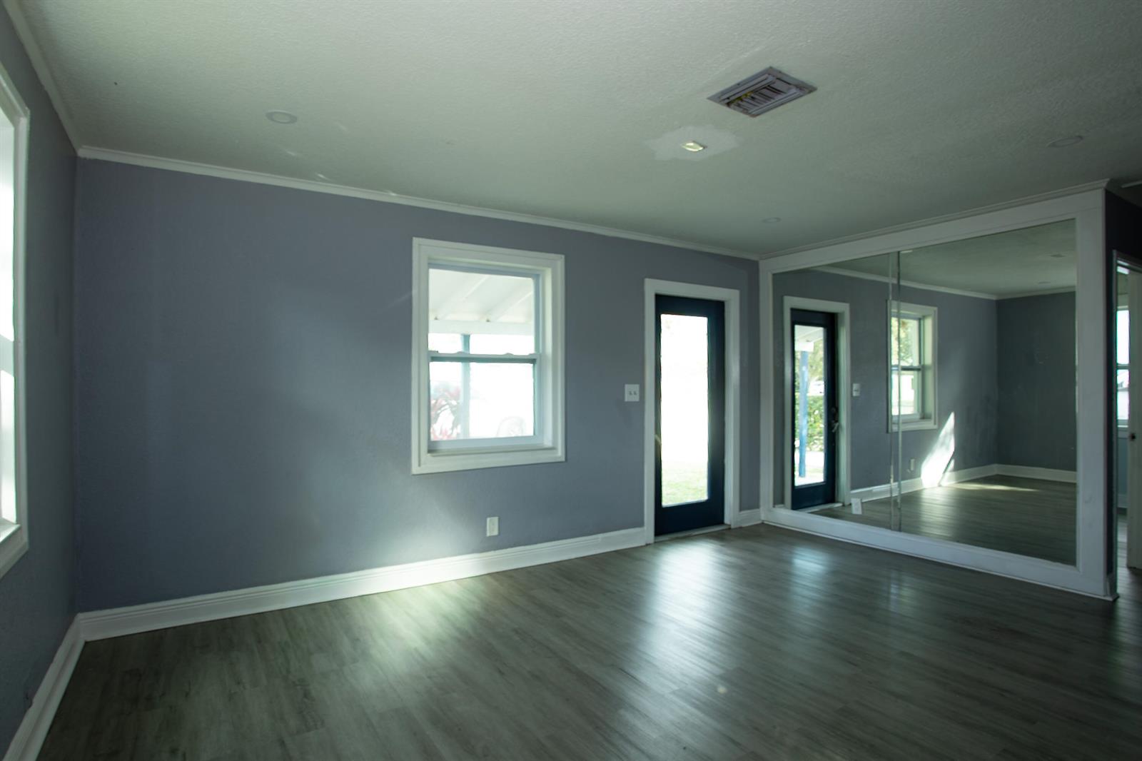 A room with gray walls, wood-look flooring, a window, a glass door, and mirrored walls — 849 W 2nd Street, Riviera Beach FL 33404, RIVIERA BEACH, FL