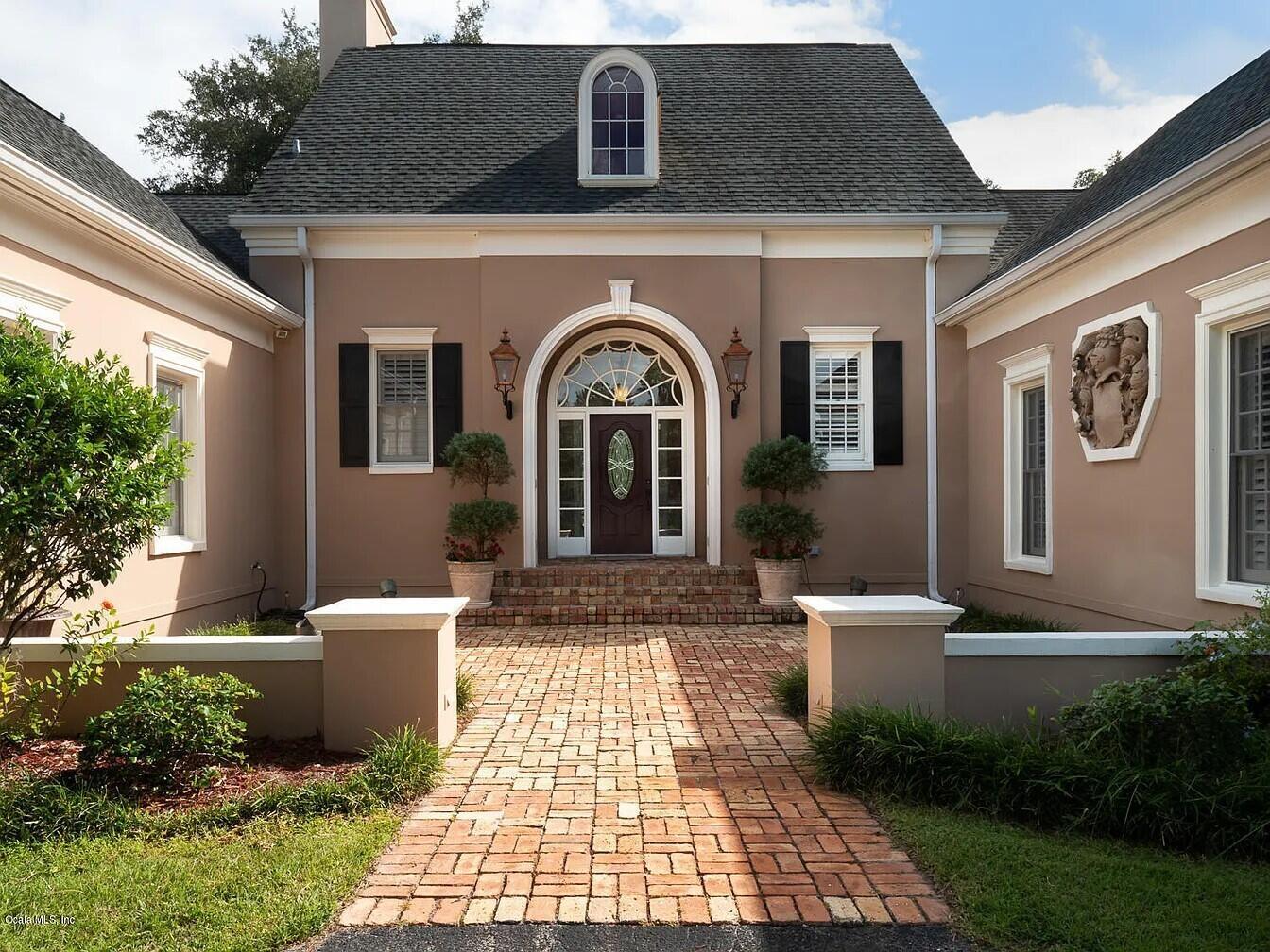 A brick walkway leads to the arched front entrance of a tan, single-story suburban home — 2030 SW 61st Lane Road, Ocala FL 34471, OCALA, FL