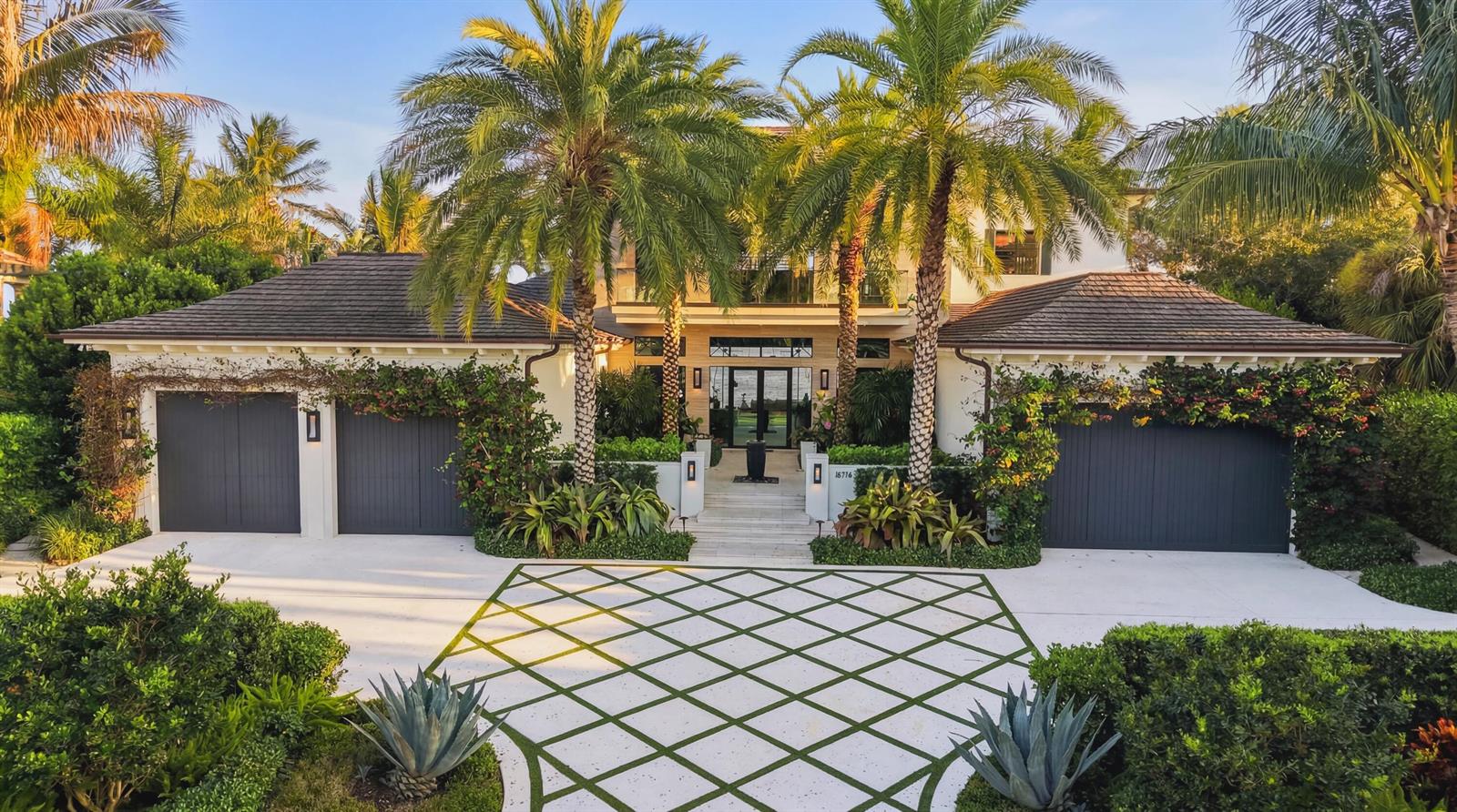 A two-story house with a diamond-patterned driveway, palm trees, and three dark garage doors — 18714 Rio Vista Drive, Jupiter FL 33469, JUPITER, FL