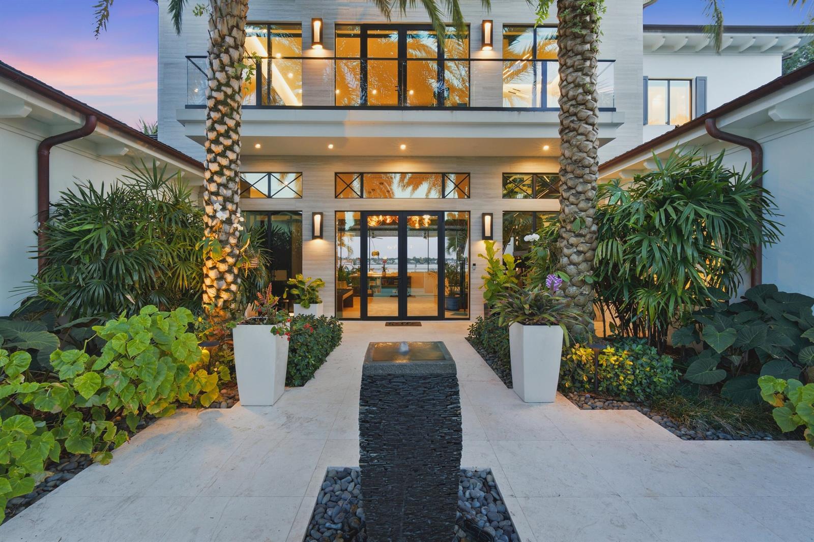 A modern house entrance features a stone fountain, palm trees, and glass-paned double doors — 18714 Rio Vista Drive, Jupiter FL 33469, JUPITER, FL