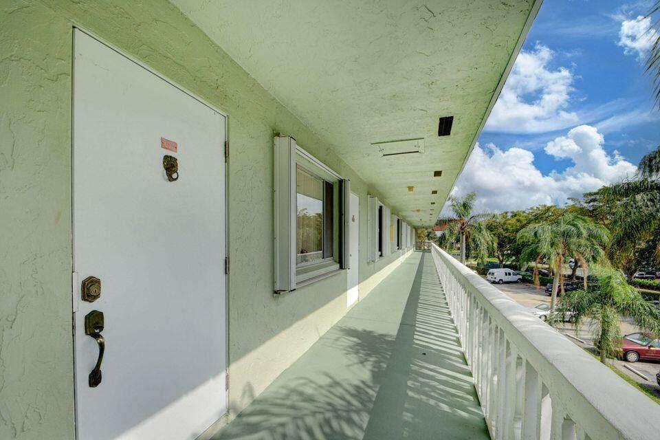 An exterior walkway with white doors and a railing overlooks a parking lot with trees — 3100 Springdale Boulevard # 310, Palm Springs FL 33461, PALM SPRINGS, FL