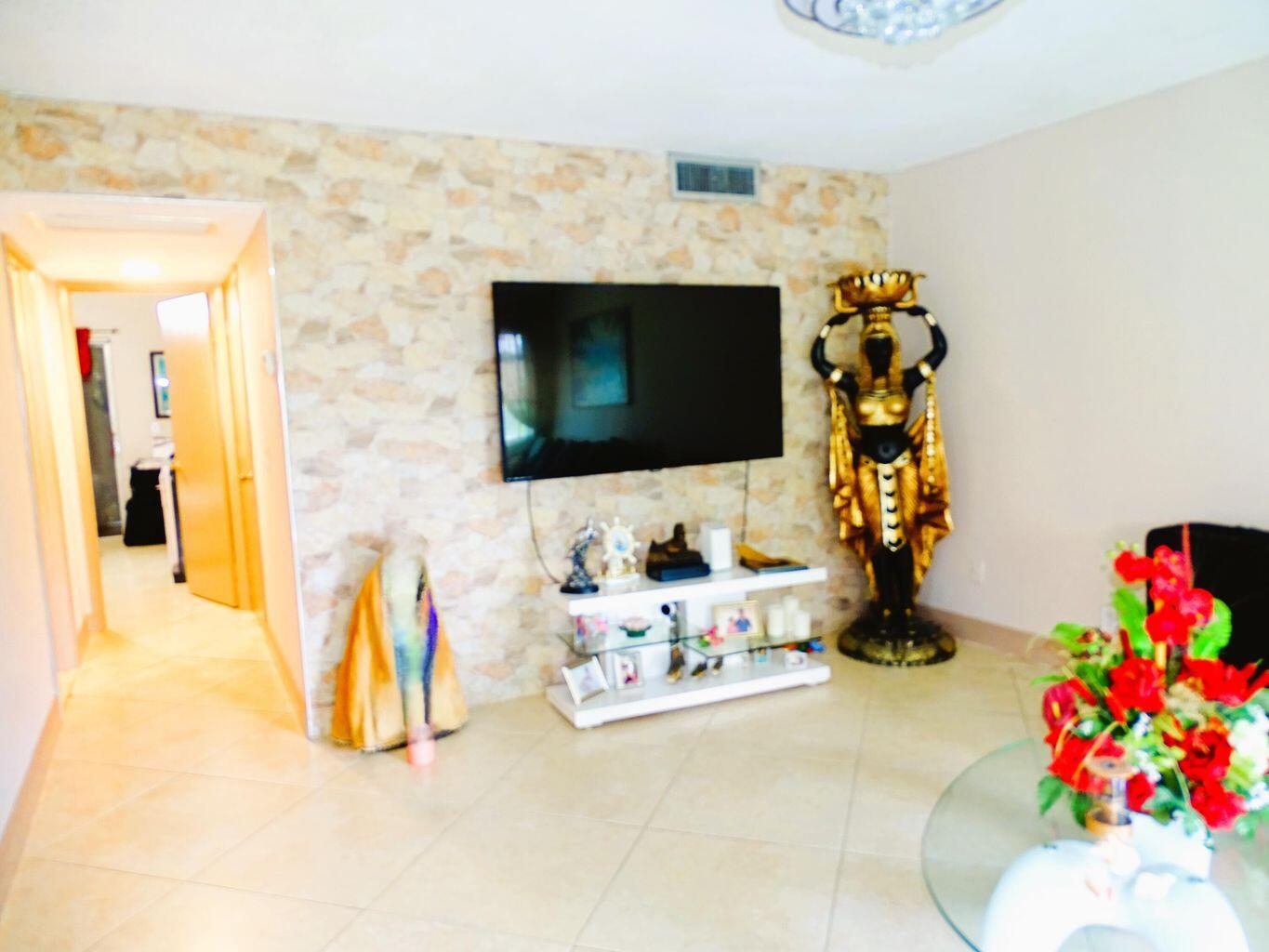 A living room features a stone accent wall, a wall-mounted television, and a decorative statue — 3100 Springdale Boulevard # 310, Palm Springs FL 33461, PALM SPRINGS, FL