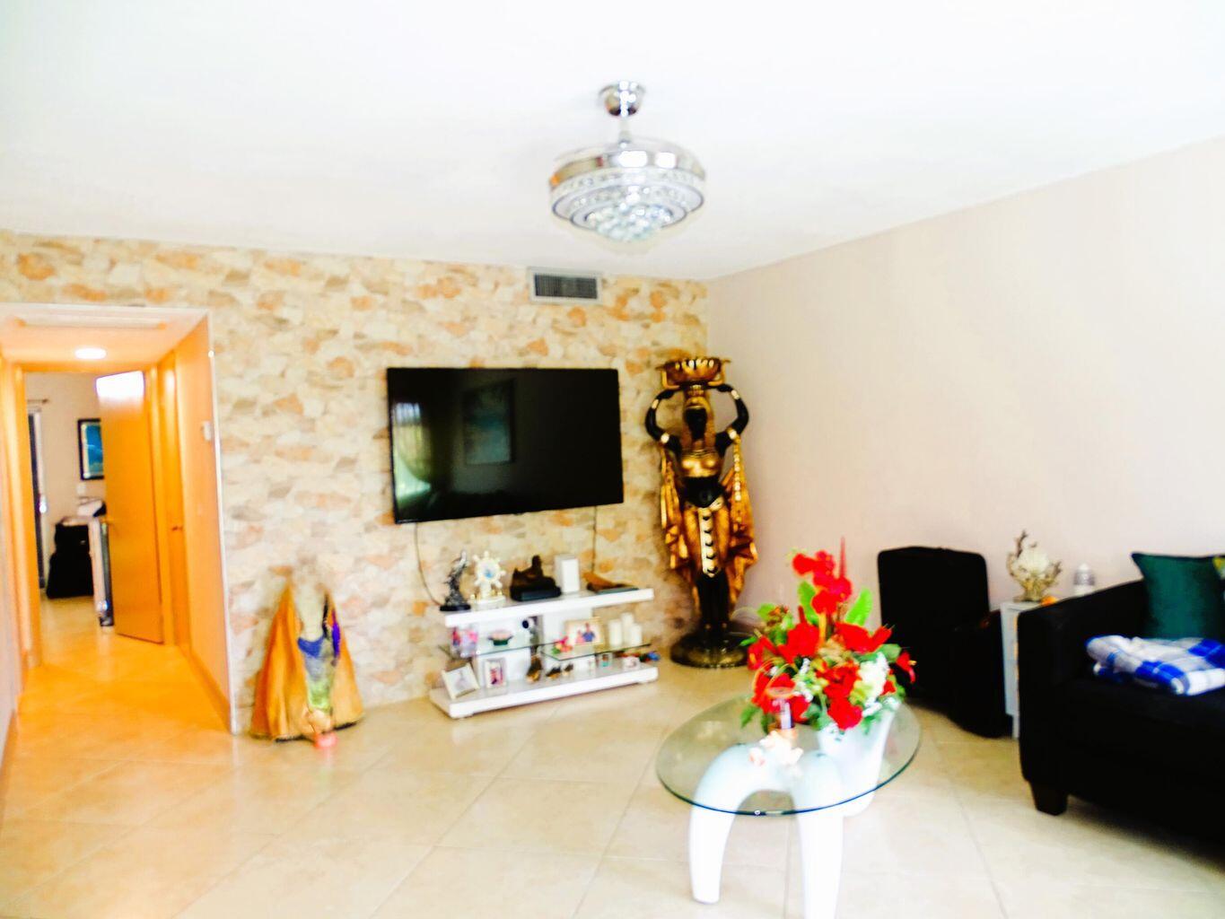 A living room features a stone accent wall, a wall-mounted television, and a glass coffee table — 3100 Springdale Boulevard # 310, Palm Springs FL 33461, PALM SPRINGS, FL