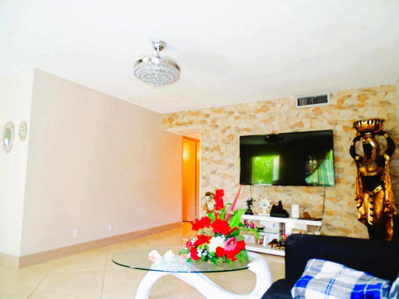 A living room features a stone accent wall, a wall-mounted television, and a glass coffee table — 3100 Springdale Boulevard # 310, Palm Springs FL 33461, PALM SPRINGS, FL