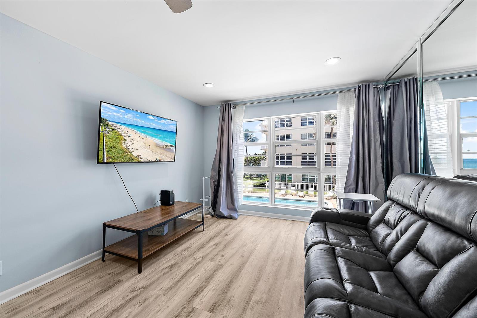 A living room features light blue walls, wood-look flooring, a wall-mounted television, and a leather sofa — 3851 N Ocean Boulevard # 202, Gulf Stream FL 33483, GULF STREAM, FL