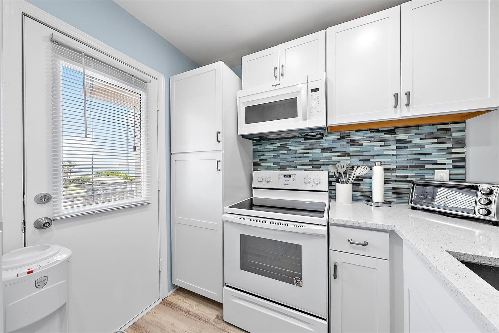 A kitchen features white cabinets, a white stove, a microwave, and a blue glass backsplash — 3851 N Ocean Boulevard # 202, Gulf Stream FL 33483, GULF STREAM, FL
