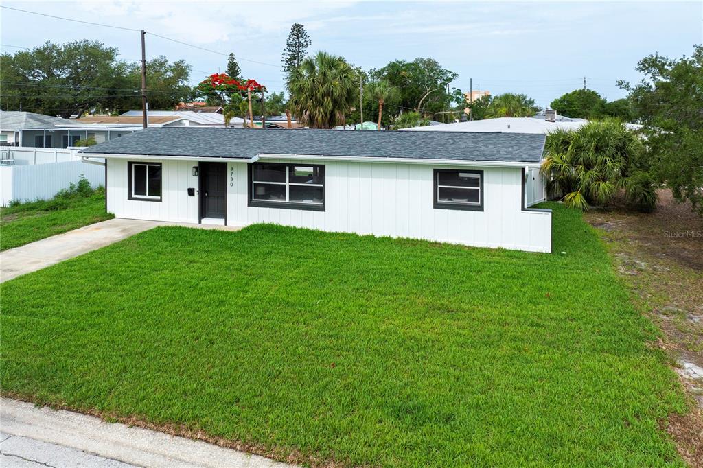 A single-story white house with a dark roof and black window frames sits on grass — 3730 75TH STREET N, ST PETERSBURG, FL