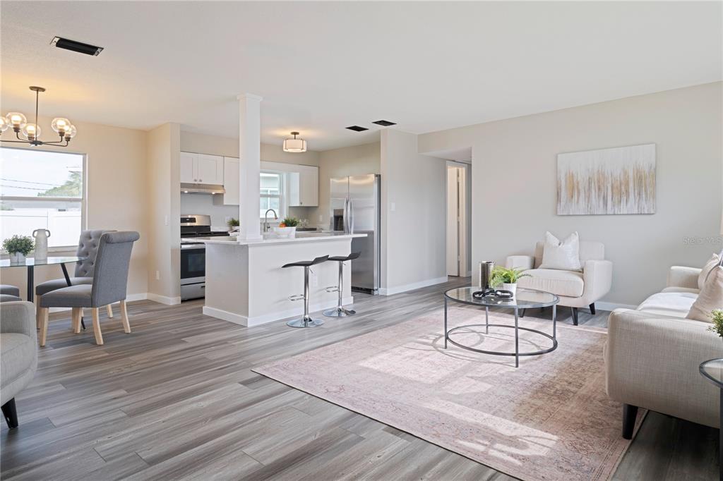 An open-concept living and dining area features gray wood-look flooring and a white kitchen island — 3730 75TH STREET N, ST PETERSBURG, FL