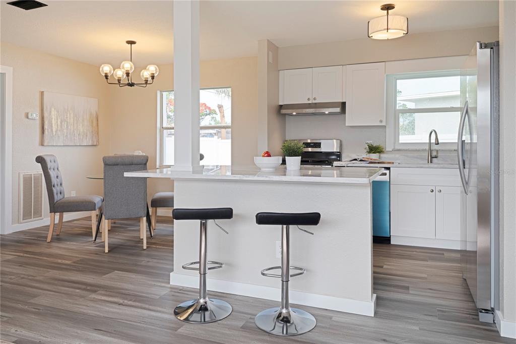 A kitchen with white cabinets, a marble-topped island, and bar stools next to a dining area — 3730 75TH STREET N, ST PETERSBURG, FL