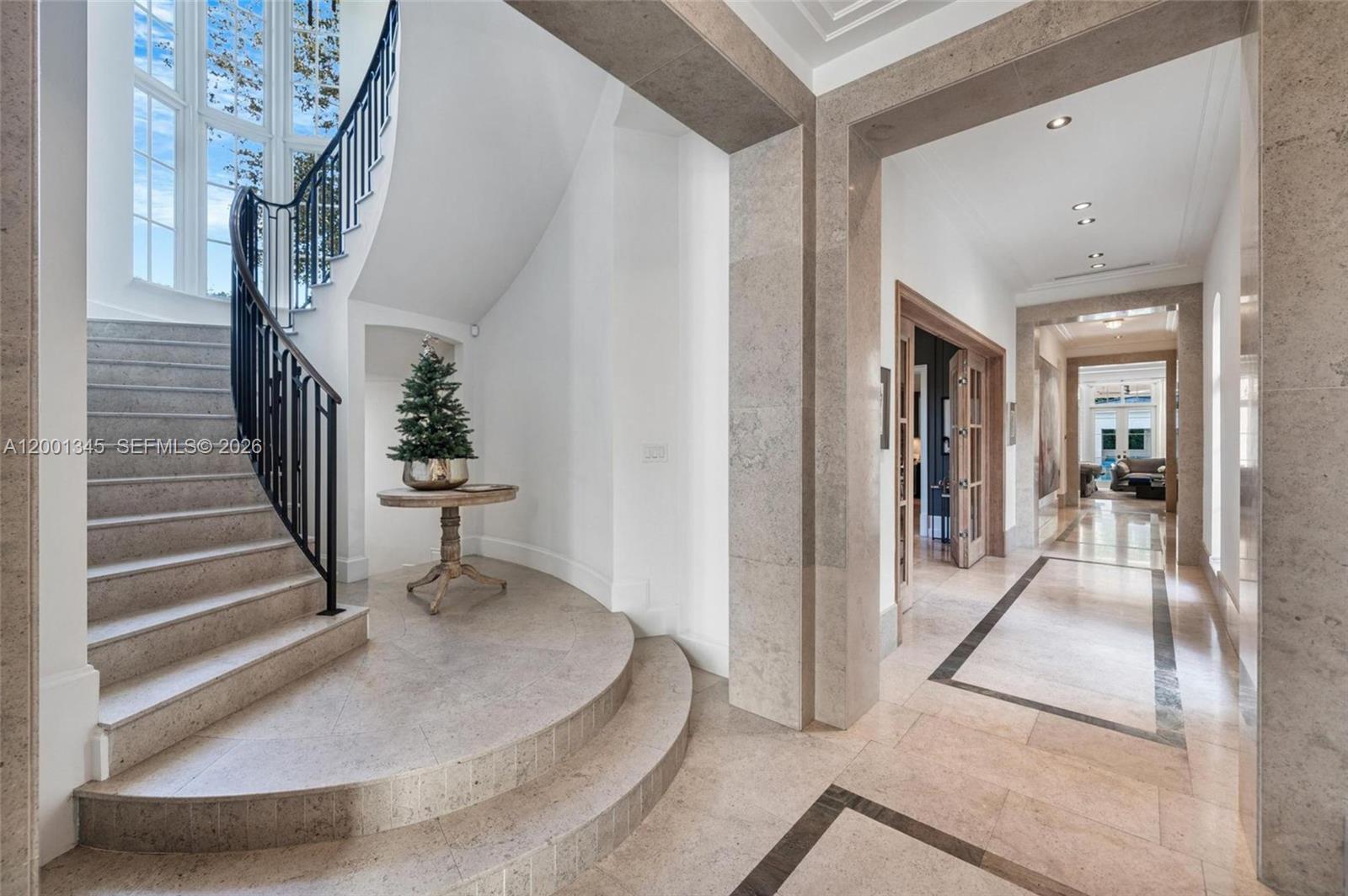 A grand foyer features a curved stone staircase, marble flooring, and a central pedestal table — 9741 W Suburban Dr, Pinecrest FL 33156, PINECREST, FL