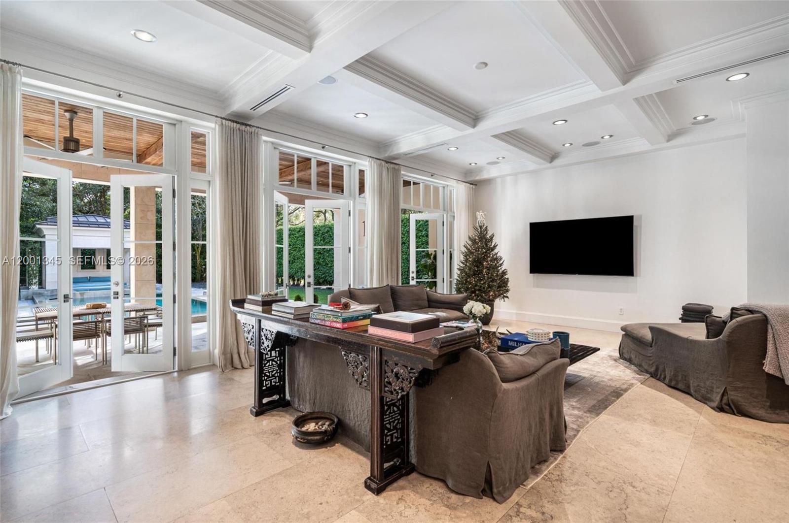 A living room with a coffered ceiling, dark sofa, ornate console table, and patio access — 9741 W Suburban Dr, Pinecrest FL 33156, PINECREST, FL