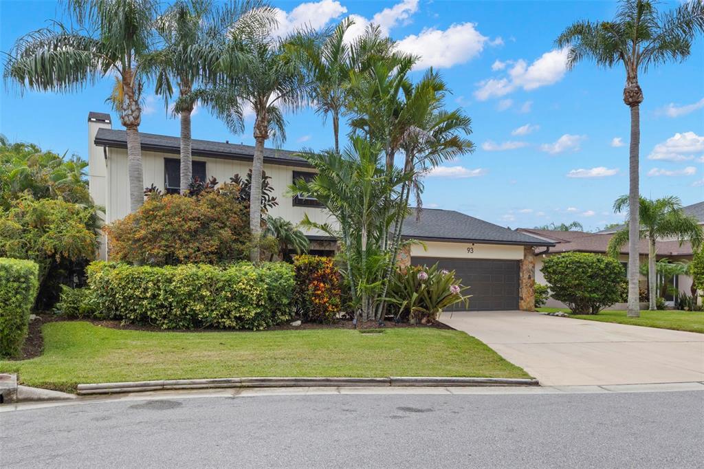 A two-story house with a garage, palm trees, and landscaping sits behind a grassy lawn — 93 S CANAL DRIVE, PALM HARBOR, FL
