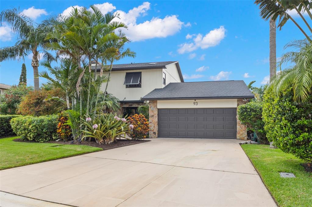 A two-story house with a stone-accented garage, a concrete driveway, and lush tropical landscaping — 93 S CANAL DRIVE, PALM HARBOR, FL