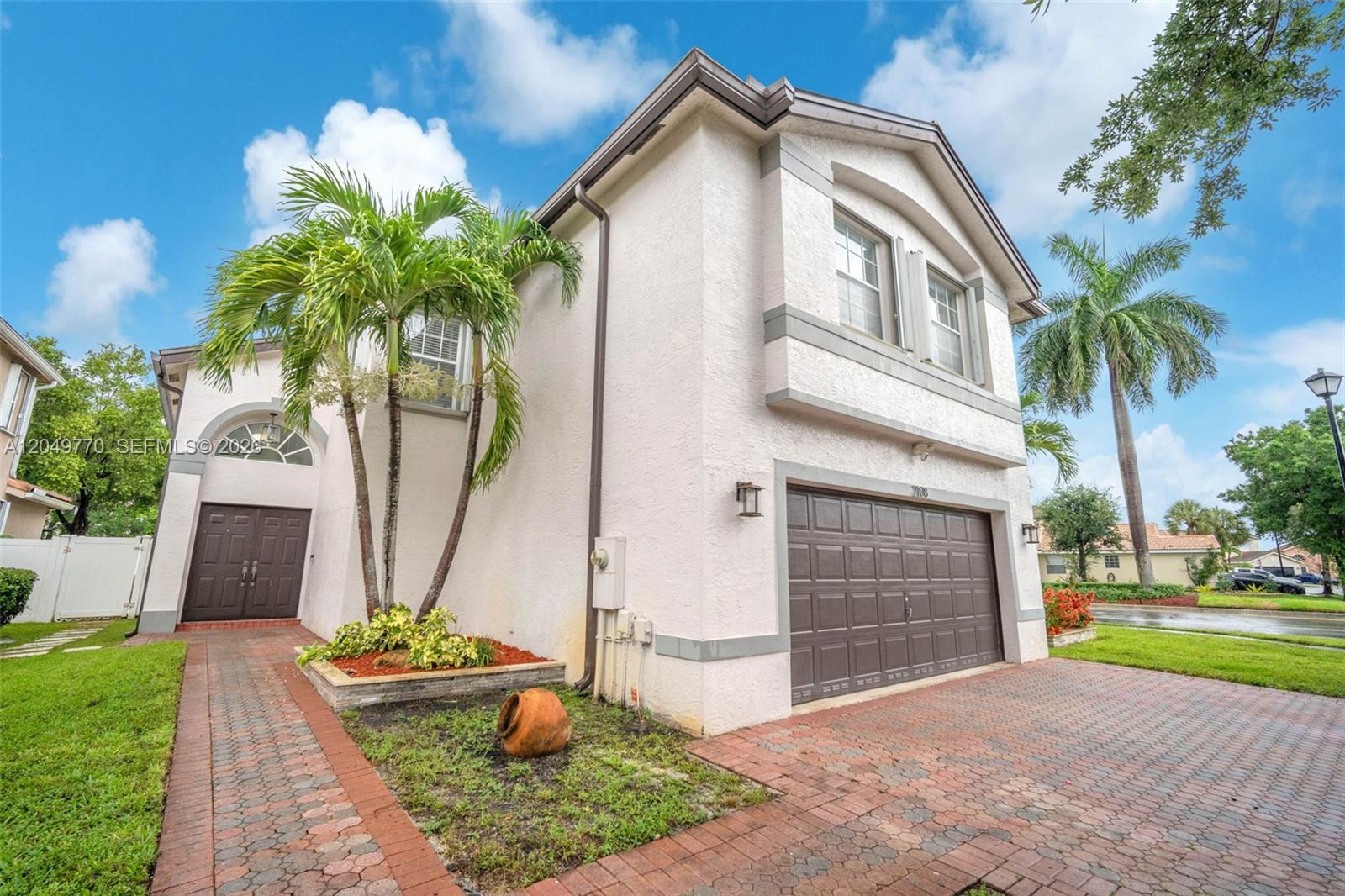 A two-story stucco house features a brown garage door, palm trees, and brick pavers — 2108 SW 151st Ave, Miramar FL 33027, MIRAMAR, FL