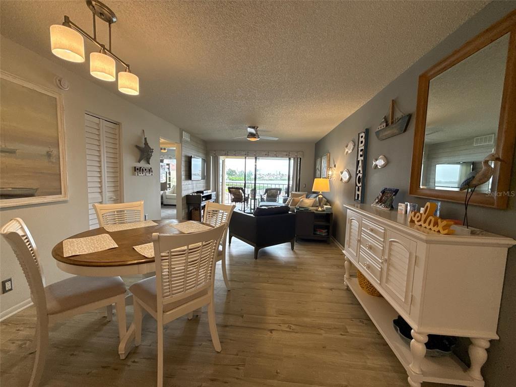 A dining area and living room with wood-look flooring, coastal decor, and a balcony view — 6158 PALMA DEL MAR BOULEVARD S UNIT 205, ST PETERSBURG, FL