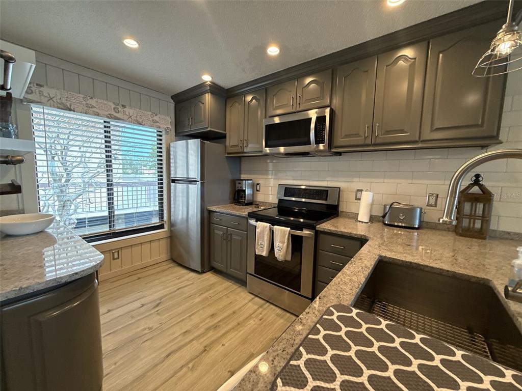 A kitchen features gray cabinets, stainless steel appliances, granite countertops, and light wood-look flooring — 6158 PALMA DEL MAR BOULEVARD S UNIT 205, ST PETERSBURG, FL