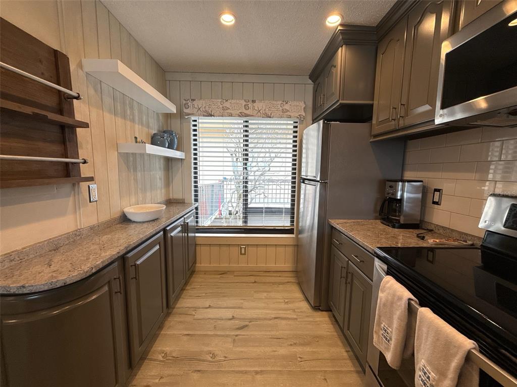 A galley kitchen features gray cabinets, granite countertops, wood-look flooring, and a window with blinds — 6158 PALMA DEL MAR BOULEVARD S UNIT 205, ST PETERSBURG, FL