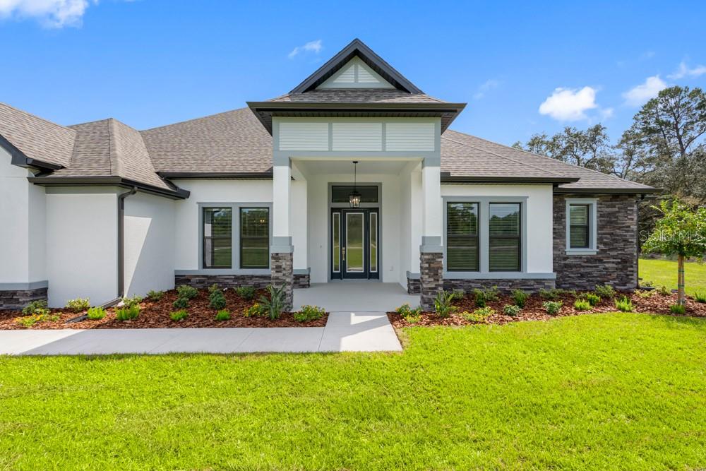The exterior of a single-story house features white stucco walls, stone accents, and a covered entryway — 17521 LIPPIZAN LANE, HUDSON, FL