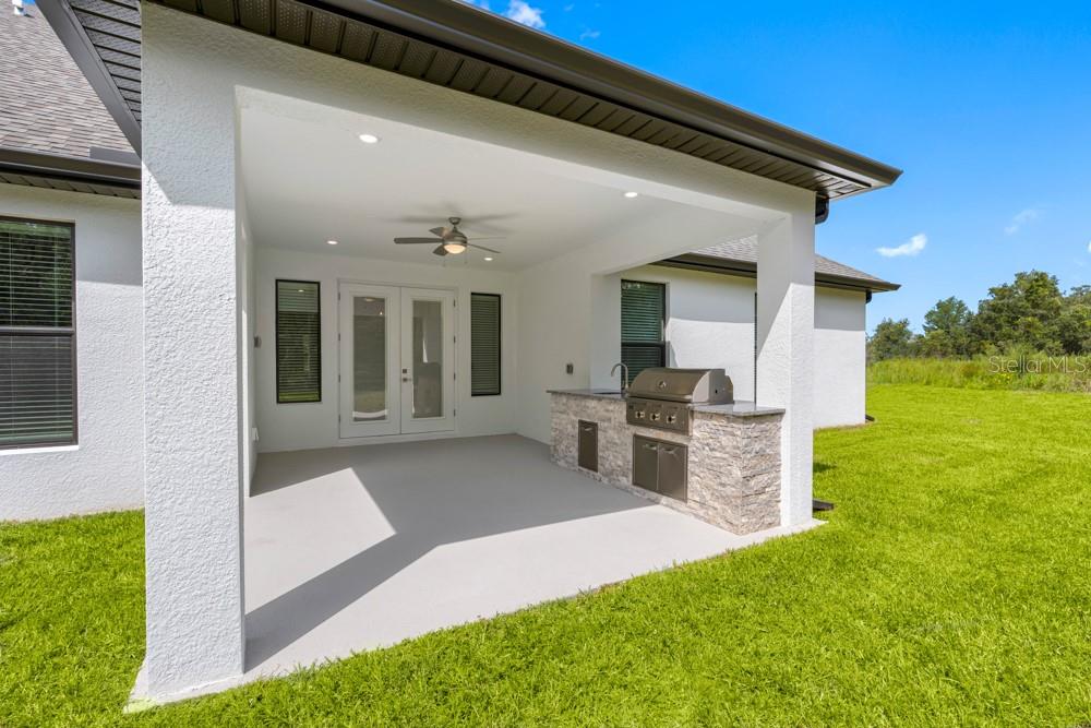 A covered outdoor patio features a built-in stone grill station and a ceiling fan — 17521 LIPPIZAN LANE, HUDSON, FL