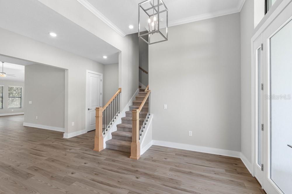 An entryway features light wood flooring, a carpeted staircase with wooden railings, and a modern chandelier — 17521 LIPPIZAN LANE, HUDSON, FL