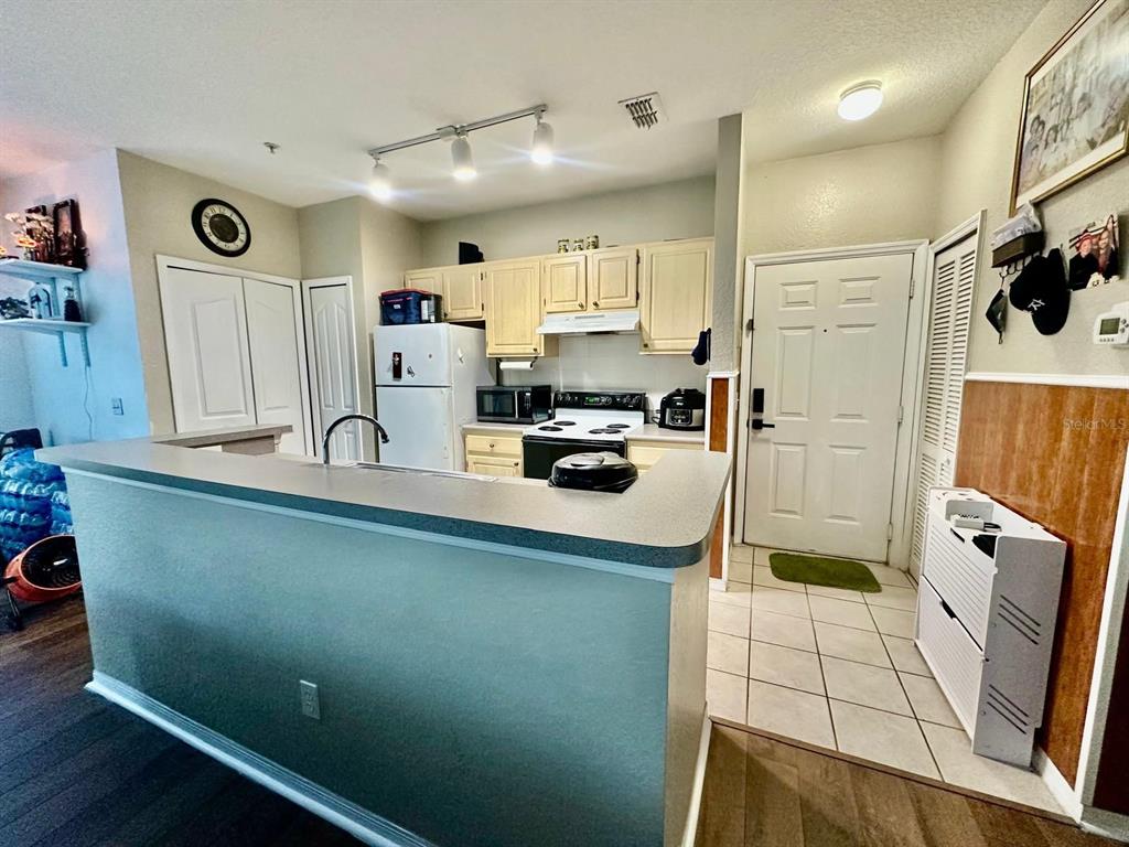 A kitchen features a breakfast bar, light-colored cabinets, white appliances, and a tiled entryway — 2718 MAITLAND CROSSING WAY UNIT 207, ORLANDO, FL