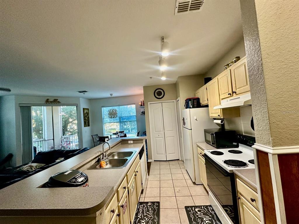 A kitchen with light-colored cabinets, a breakfast bar, and tile flooring opens to a living area — 2718 MAITLAND CROSSING WAY UNIT 207, ORLANDO, FL
