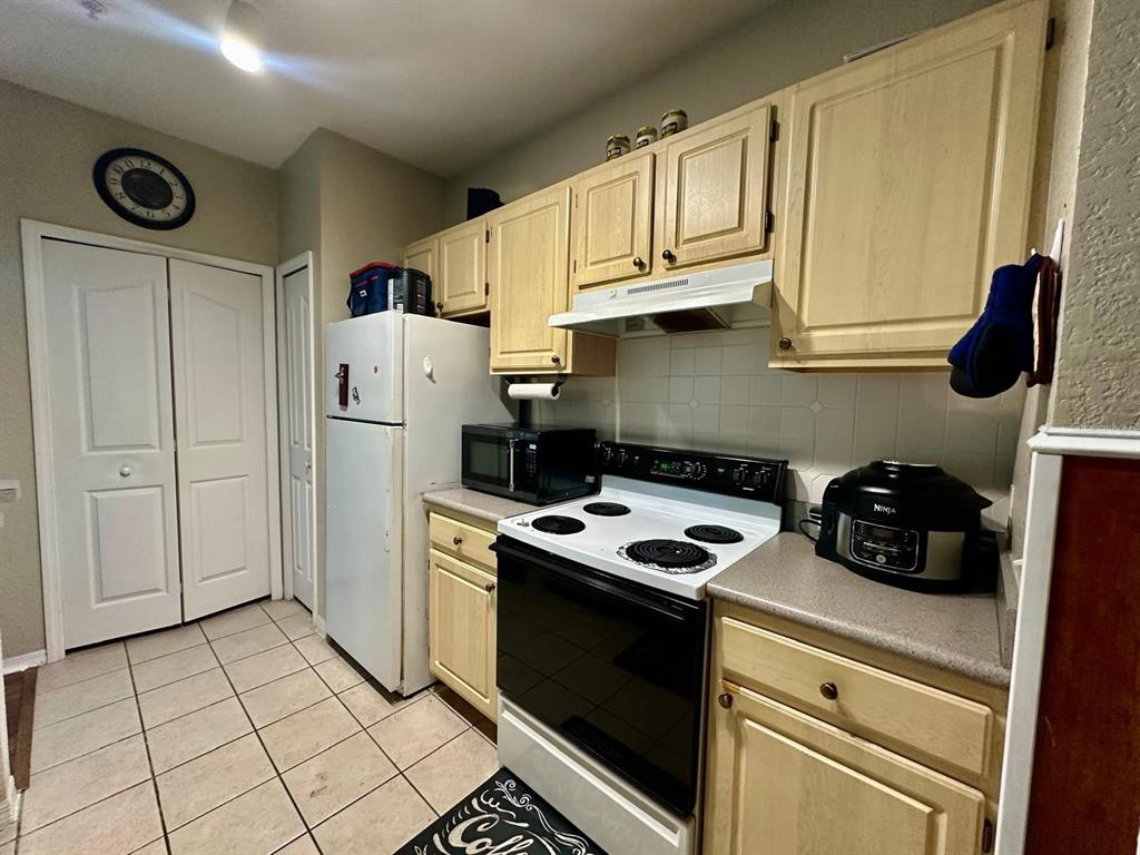 A kitchen features light wood cabinets, white appliances, a tiled floor, and a wall clock — 2718 MAITLAND CROSSING WAY UNIT 207, ORLANDO, FL