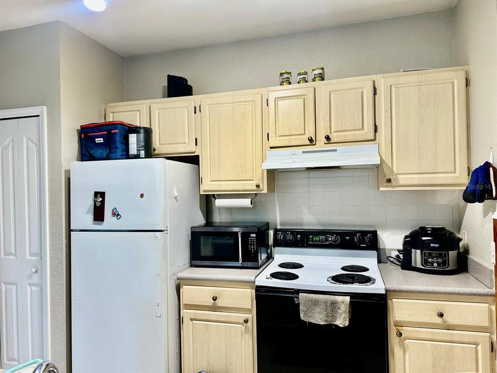 A kitchen features light wood cabinets, white appliances, and a tiled backsplash — 2718 MAITLAND CROSSING WAY UNIT 207, ORLANDO, FL